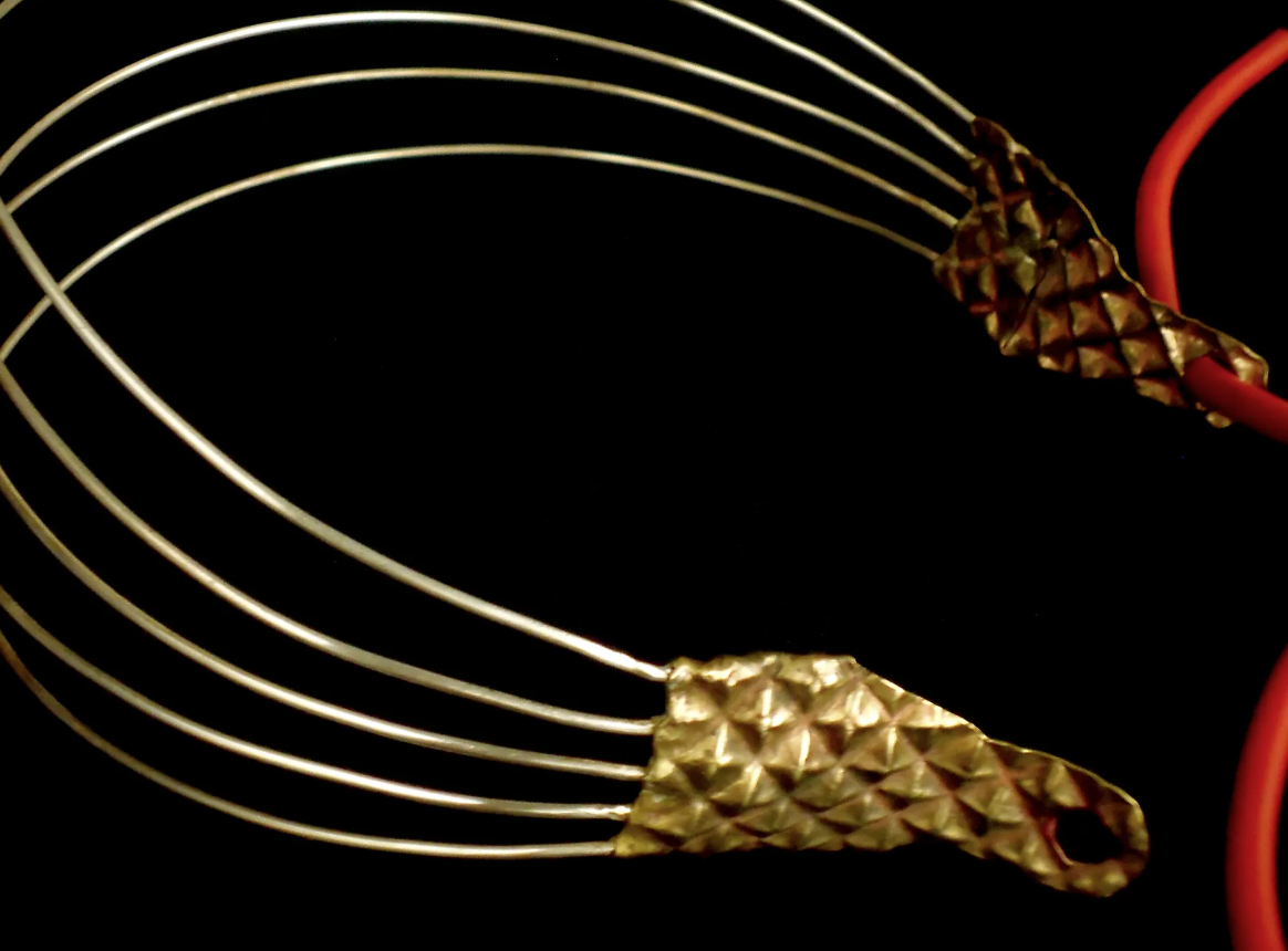 Close-up of a decorative metallic wire headband with a textured gold embellishment on each end, set against a black background.