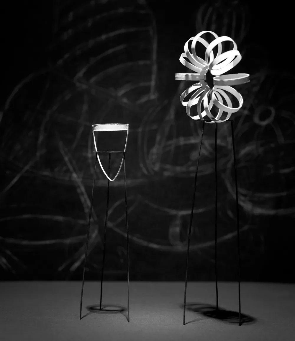 Two abstract sculptures made of metal wires with geometric shapes, set against a dark background.