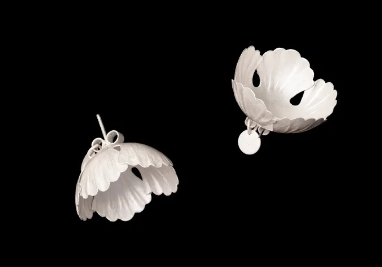 Two white organic-shaped earrings suspended in mid-air against a black background.