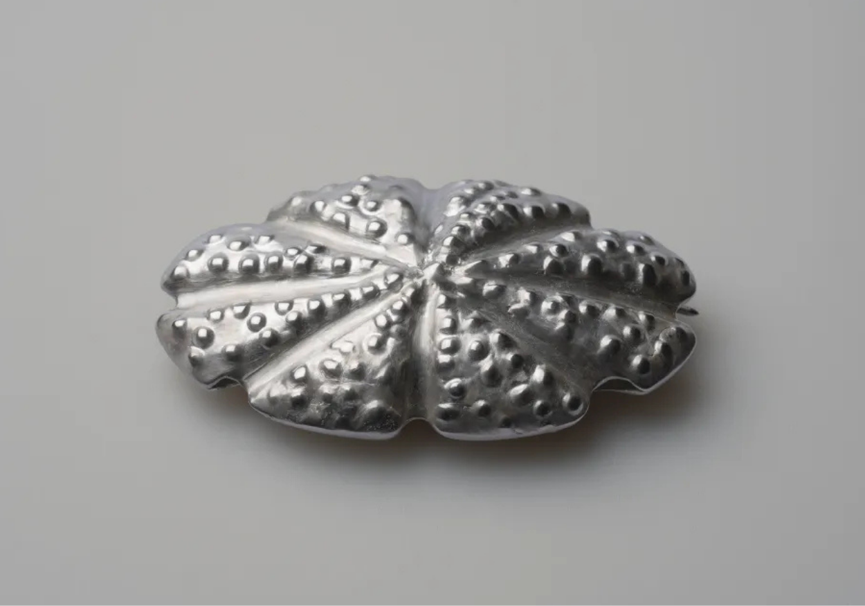 Silver metallic decorative brooch with embossed dot pattern on a plain white background.