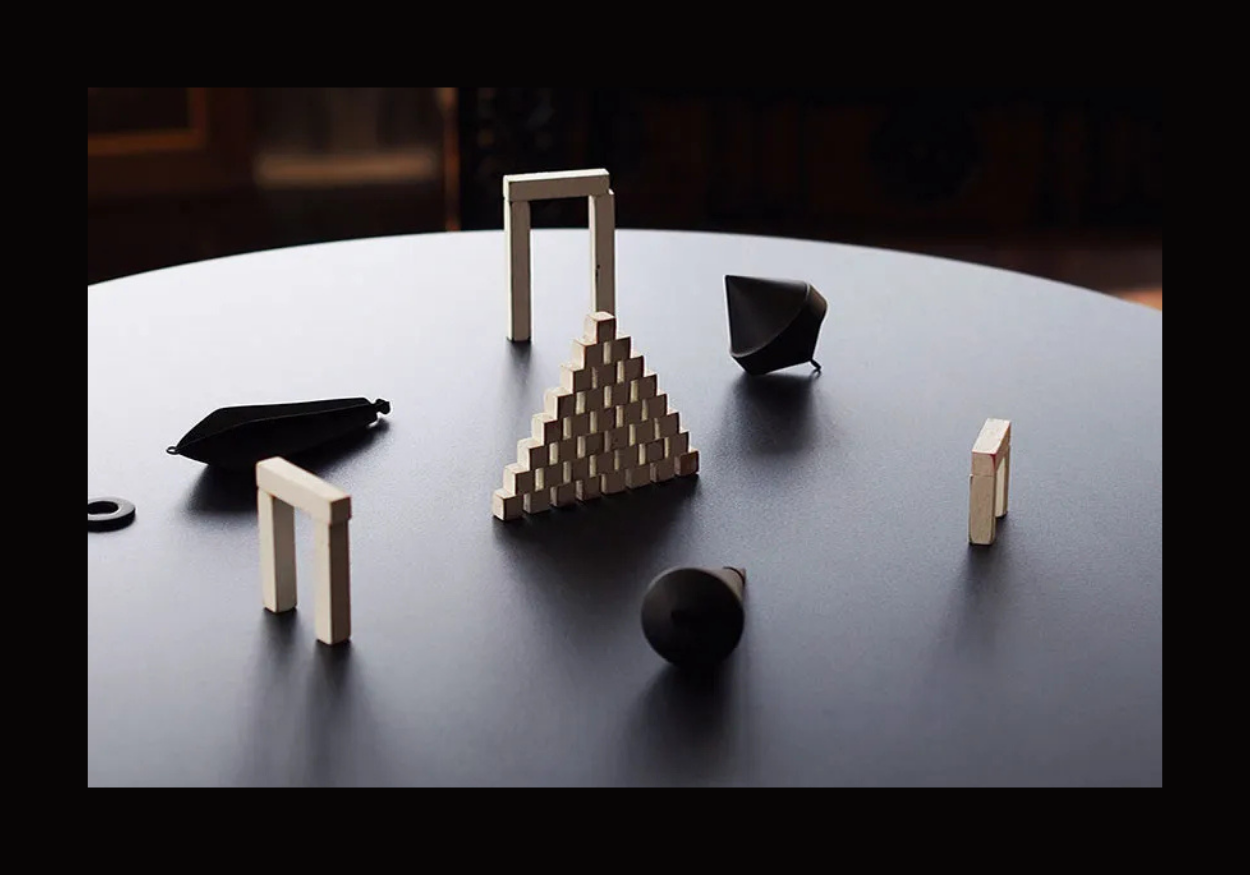 Various black and white pieces and wooden blocks on a dark tabletop, arranged in a circle.