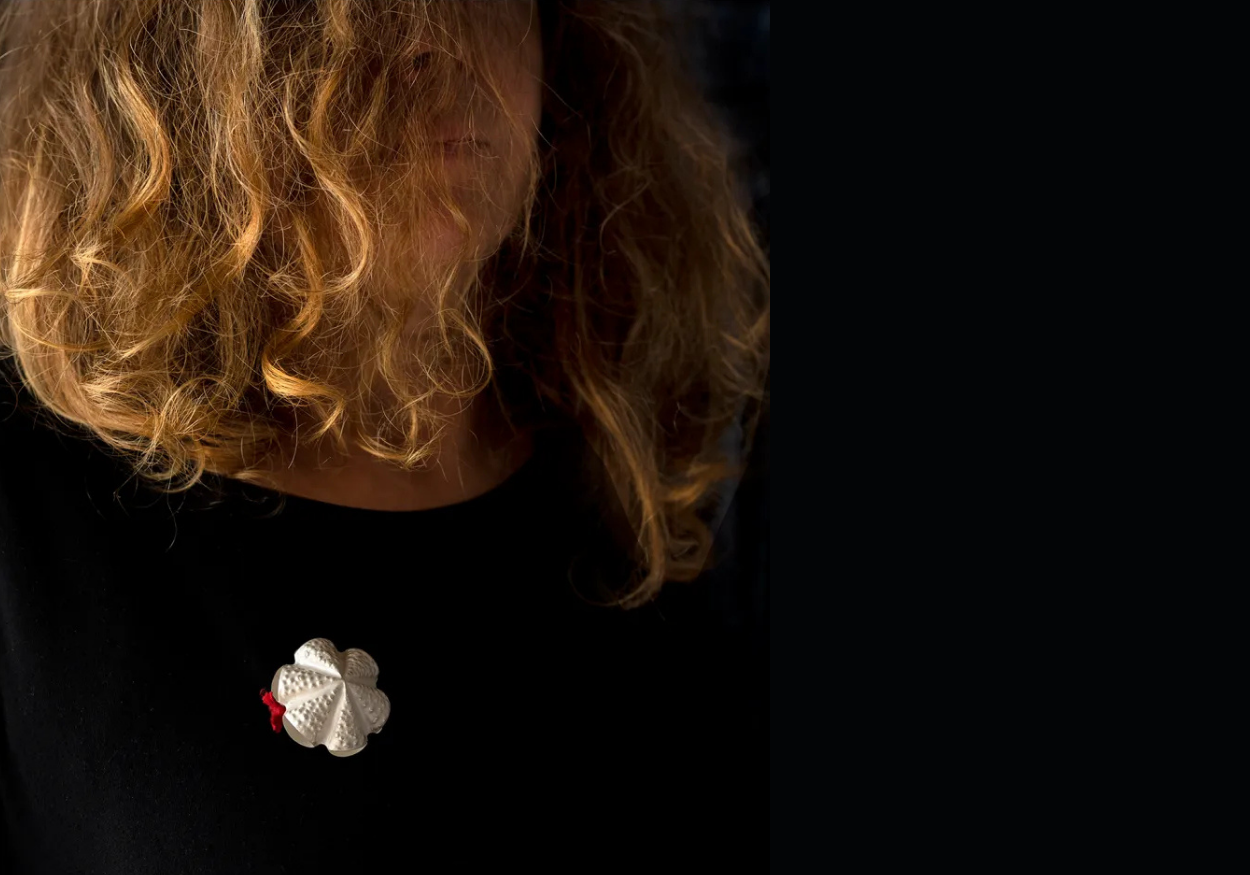 Close-up of a woman with curly blonde hair wearing a black top and a white decorative brooch.