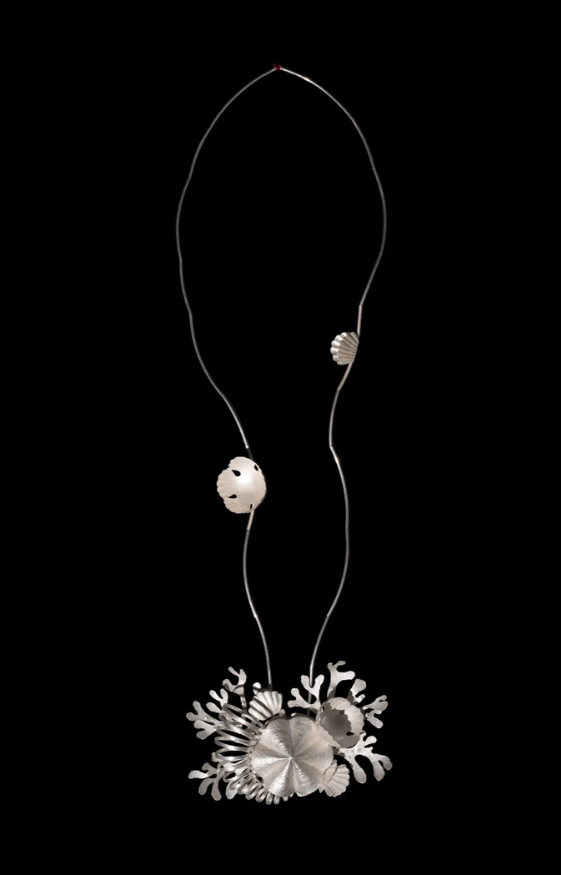 A modern silver necklace with shell and coral-like pendant design against a black background.