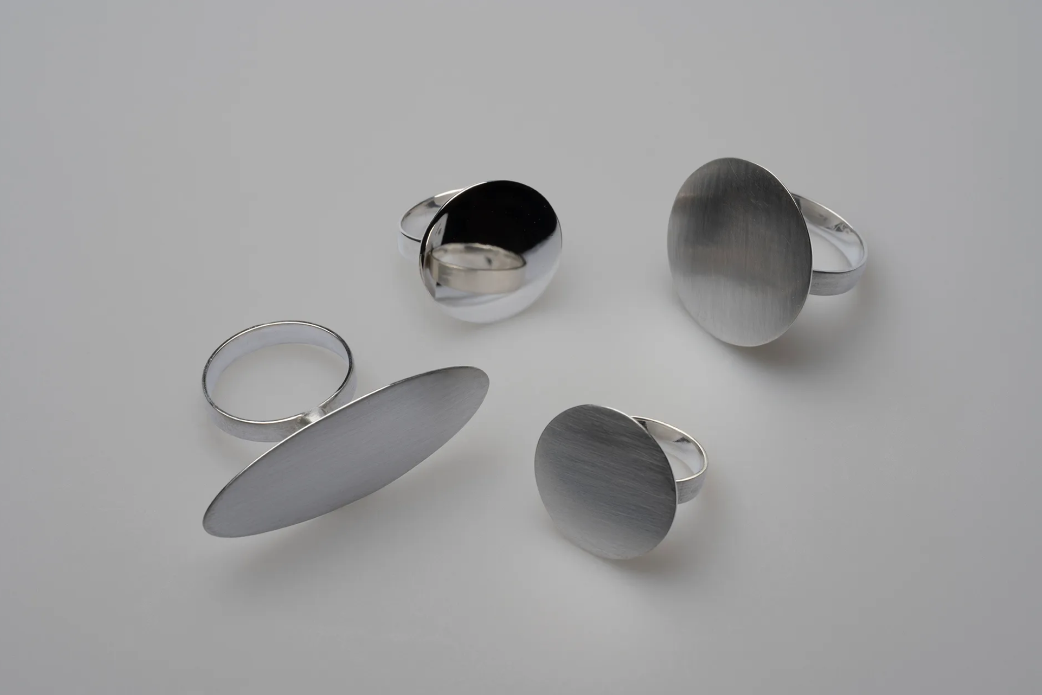 Multiple silver jewellery pieces, including rings and oval-shaped pendants, on a white surface.