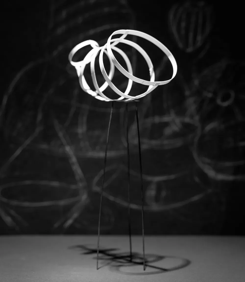 A modern art sculpture of three illuminated metal rings connected together, casting shadows on a dark background.