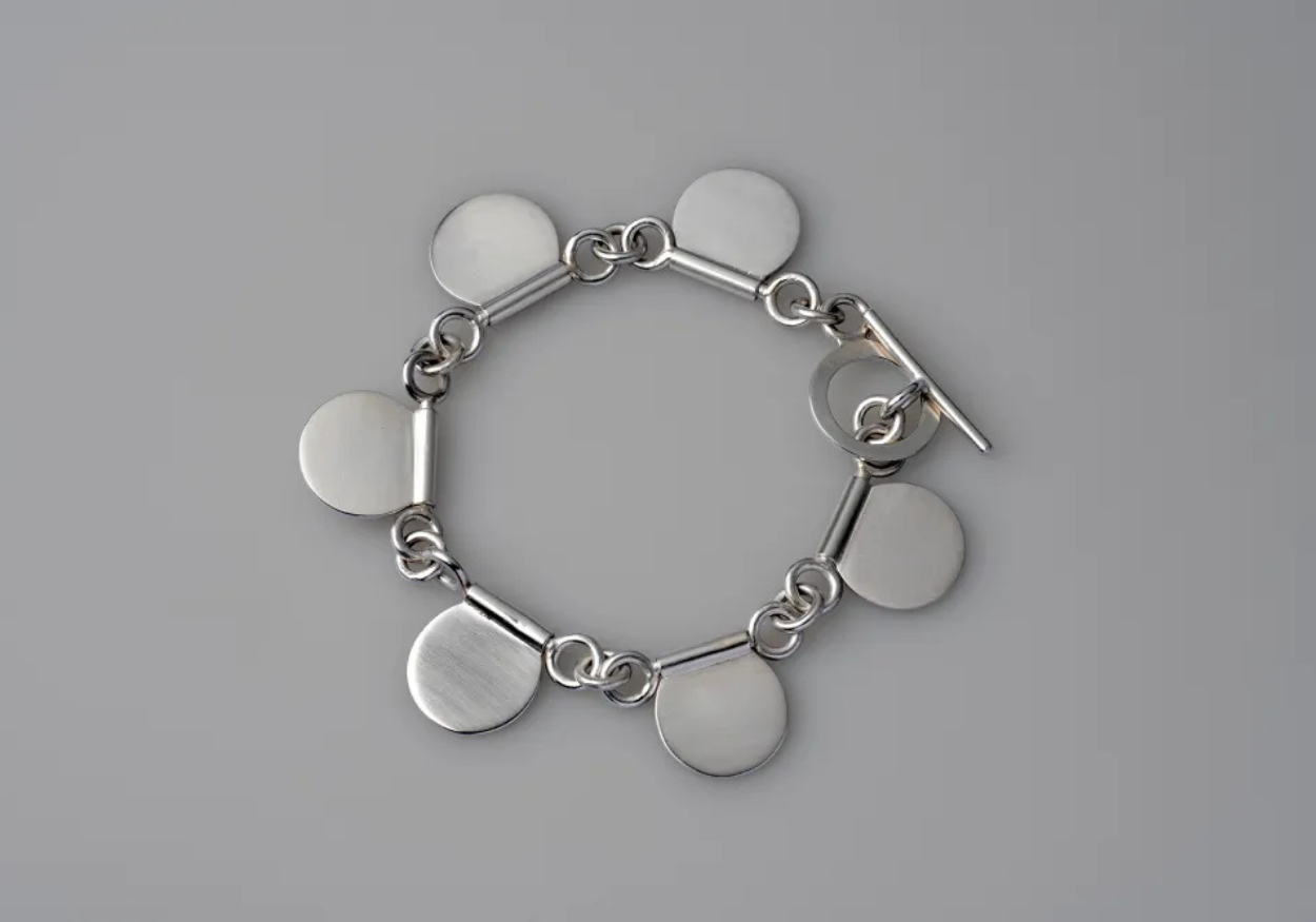 Silver bracelet with circular and bar-shaped charms on a gray background.