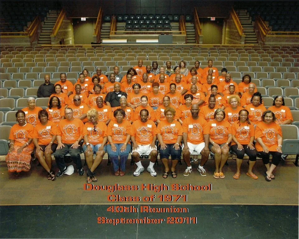 Group photo of Douglass High School classmates wearing orange shirts, seated in an auditorium with empty seats in the background. The image is captioned: 'Douglass High School Class of 1971 40th Reunion September 2011'.