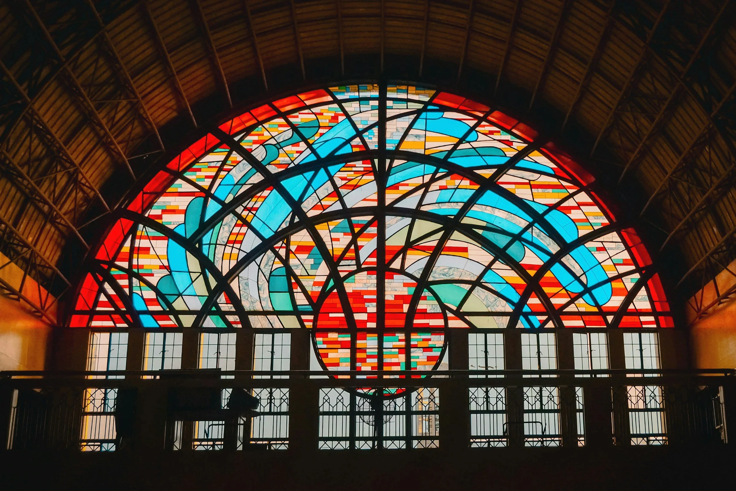 Colorful stained glass window with abstract patterns and a large circle at the center, inside a wooden arched ceiling
