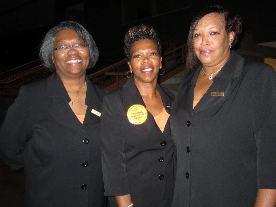Three women in black uniforms standing together at an indoor event.