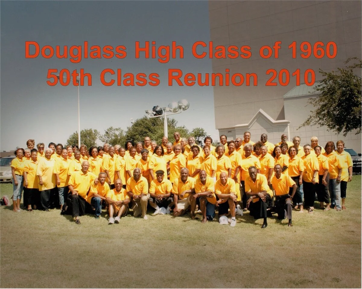 Group photo of Douglass High School 1960 alumni in yellow shirts at their 50th class reunion in 2010, outdoors on grass with trees and building in background.
