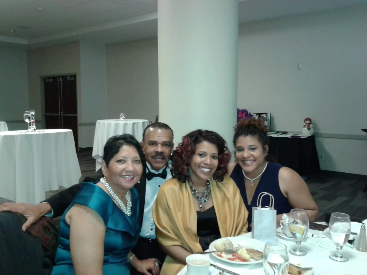 Four people sitting at a round table smiling at a camera in a banquet hall.