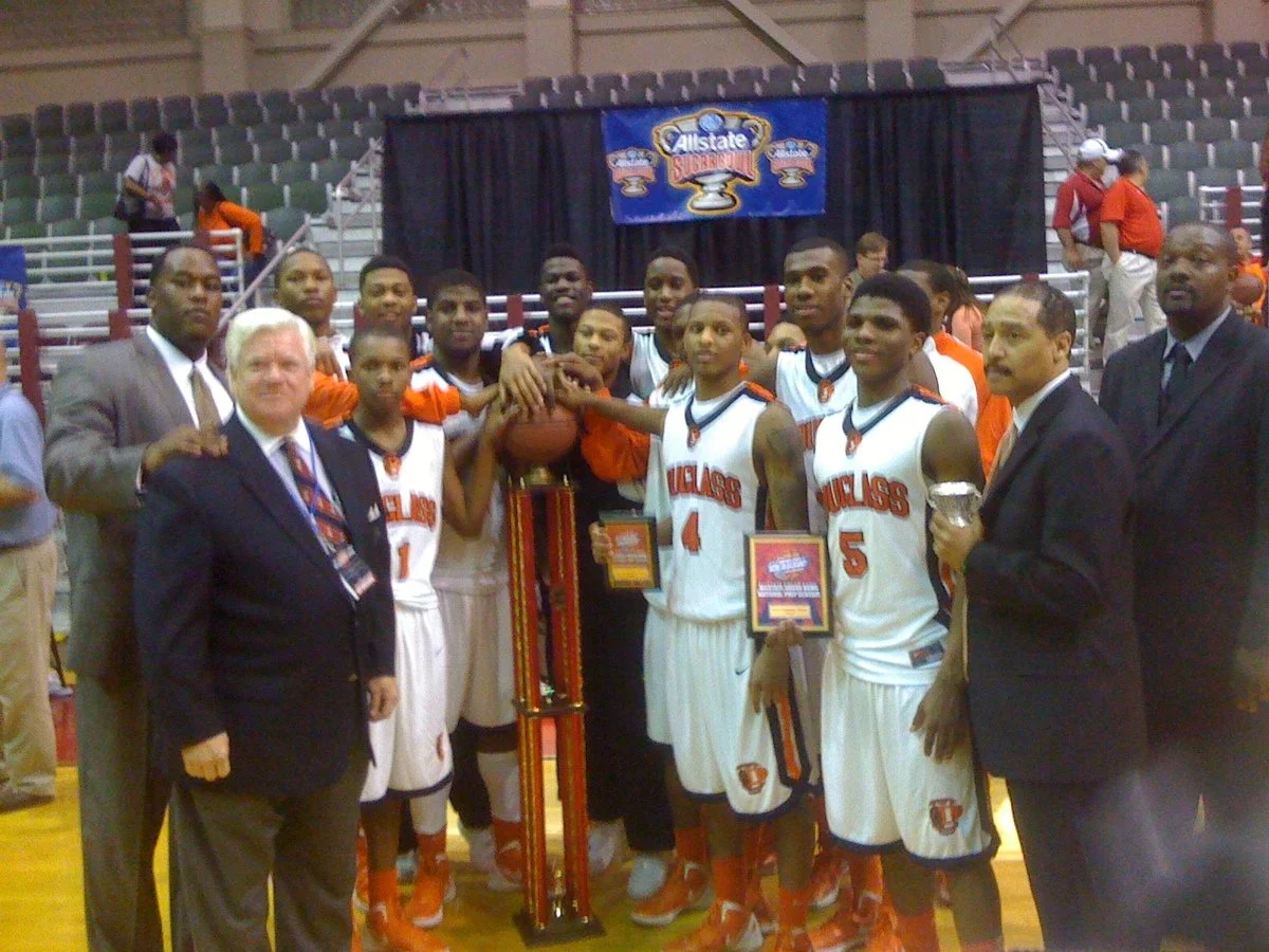 Basketball team in white and orange uniforms celebrating with a trophy and plaques in an indoor gymnasium, with coaches and officials, at an Allstate Sugar Bowl event.