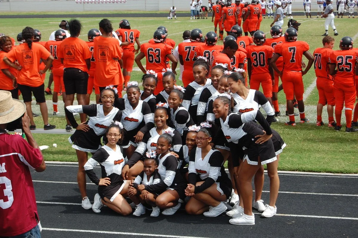 Group of young cheerleaders smiling in uniforms in front of football team on field