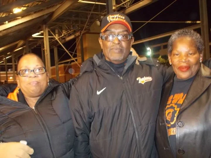 Three people standing together outdoors at night, two women and one man, all wearing dark jackets and smiling for the camera.