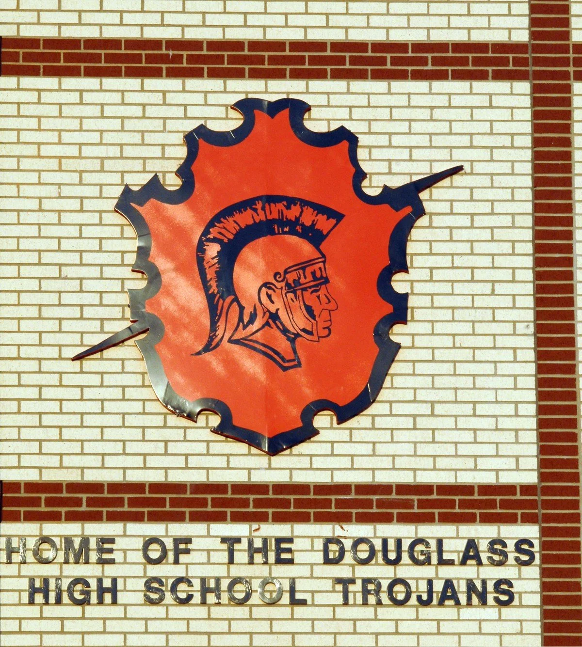School sign with a large orange emblem featuring a Trojan helmet, and text below that reads "Home of the Douglass High School Trojans."