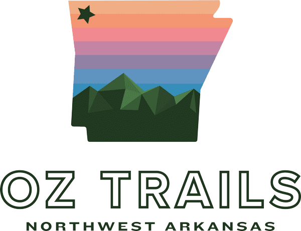 Stylized Arkansas map with a rainbow gradient, green mountains, and a star, with text 'Oz Trails Northwest Arkansas'.