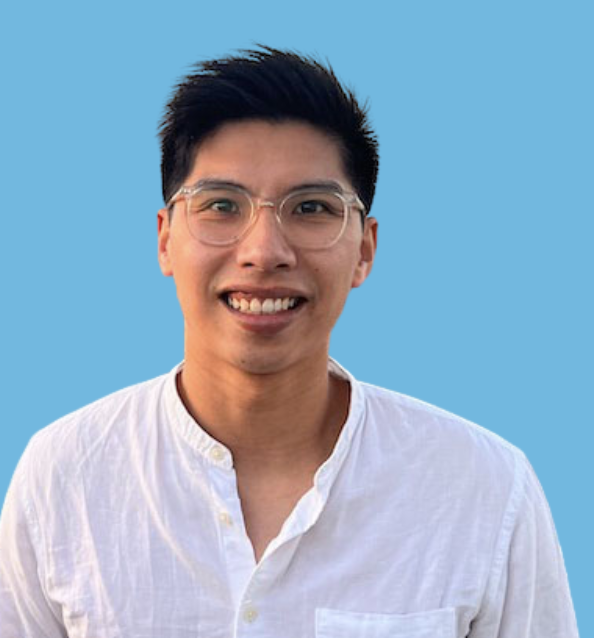 A smiling young man with glasses, short black hair, wearing a white button-down shirt, standing against a blue background.