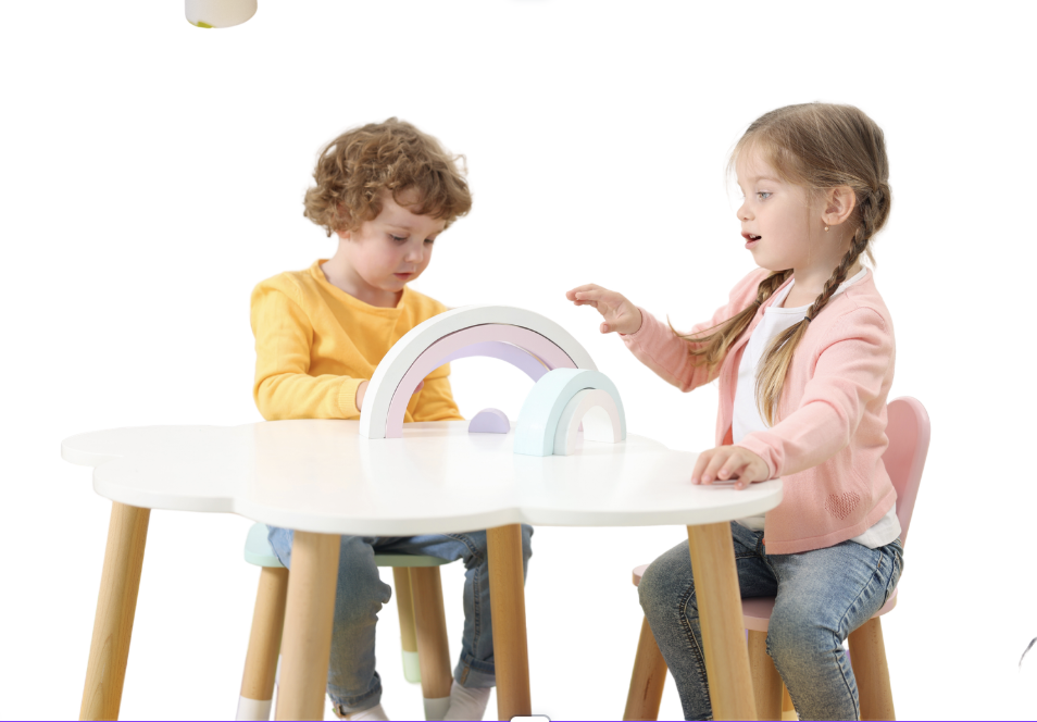 Two young children, a boy and a girl, sit at a white table playing with pastel-colored rainbow-shaped toys.