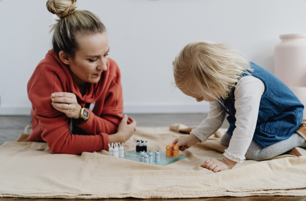 A woman and a young girl playing a board game on a beige blanket.