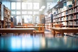 Empty library with tall bookshelves, wooden tables and chairs, and large windows letting in natural light.