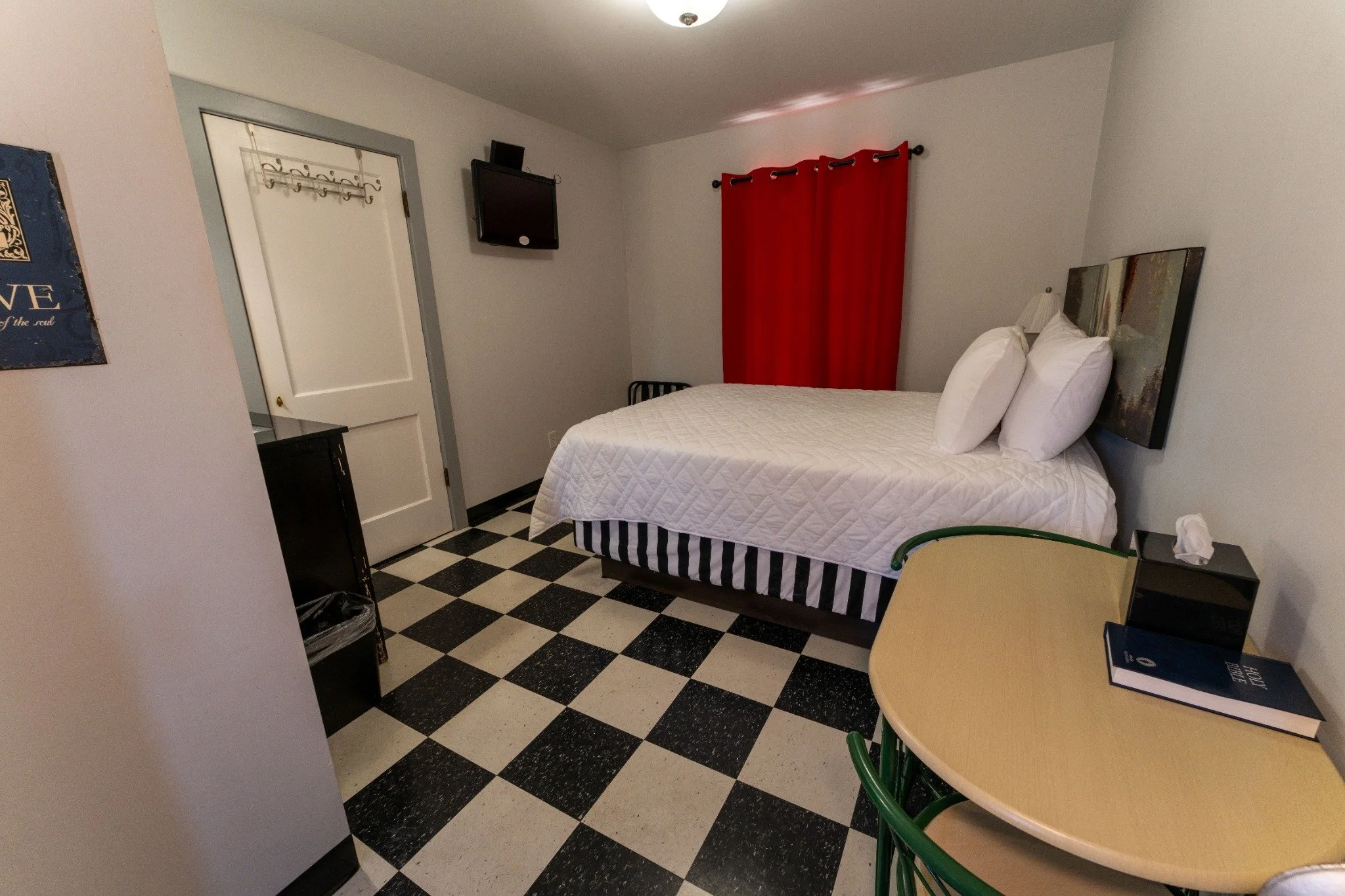Bright Wagon Wheel Motel guest room with a bed, black-and-white tile floor, writing table, and red curtains.