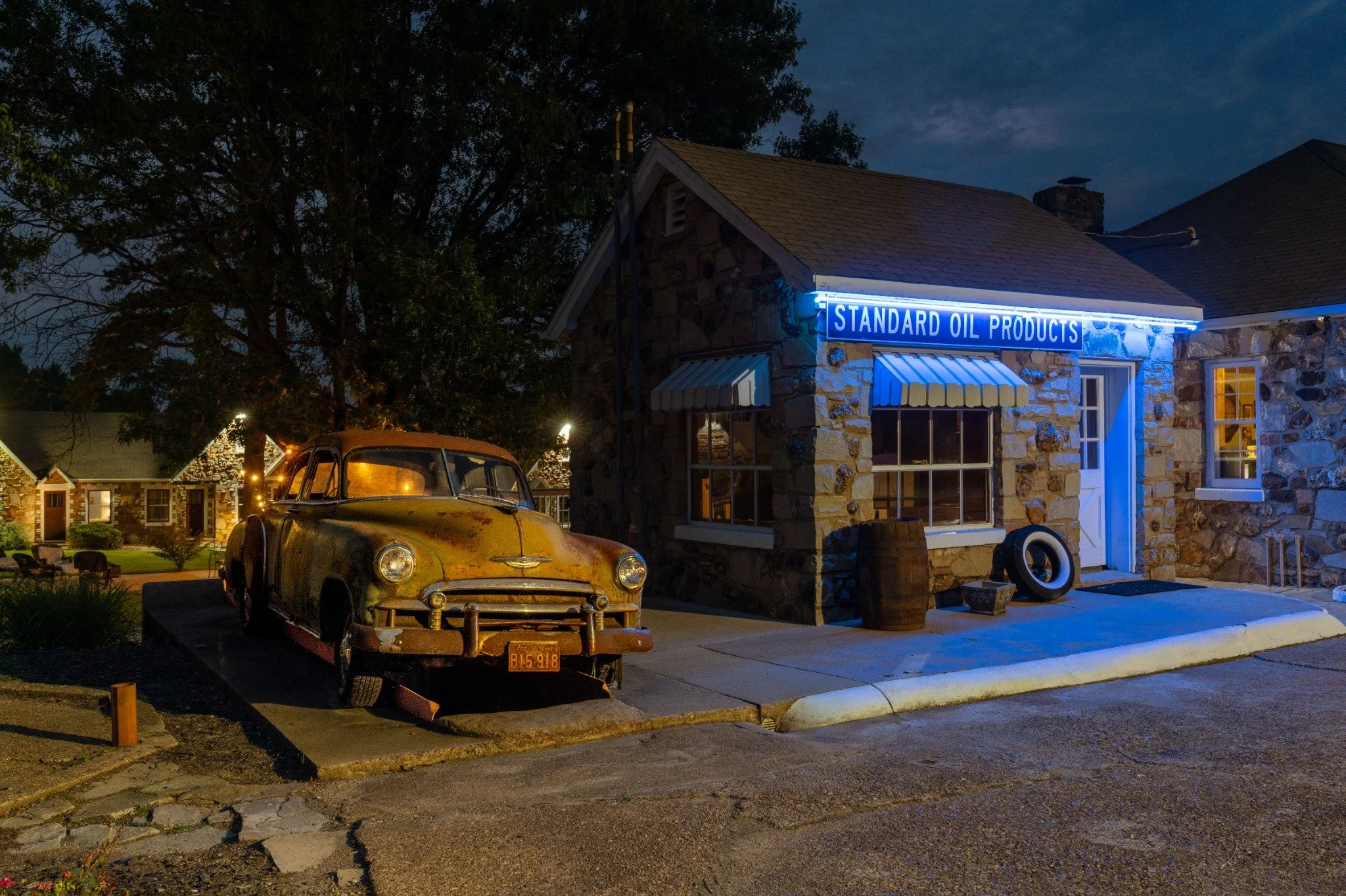 Classic Chevrolet parked beside the illuminated Wagon Wheel Motel stone office and Standard Oil sign at night.