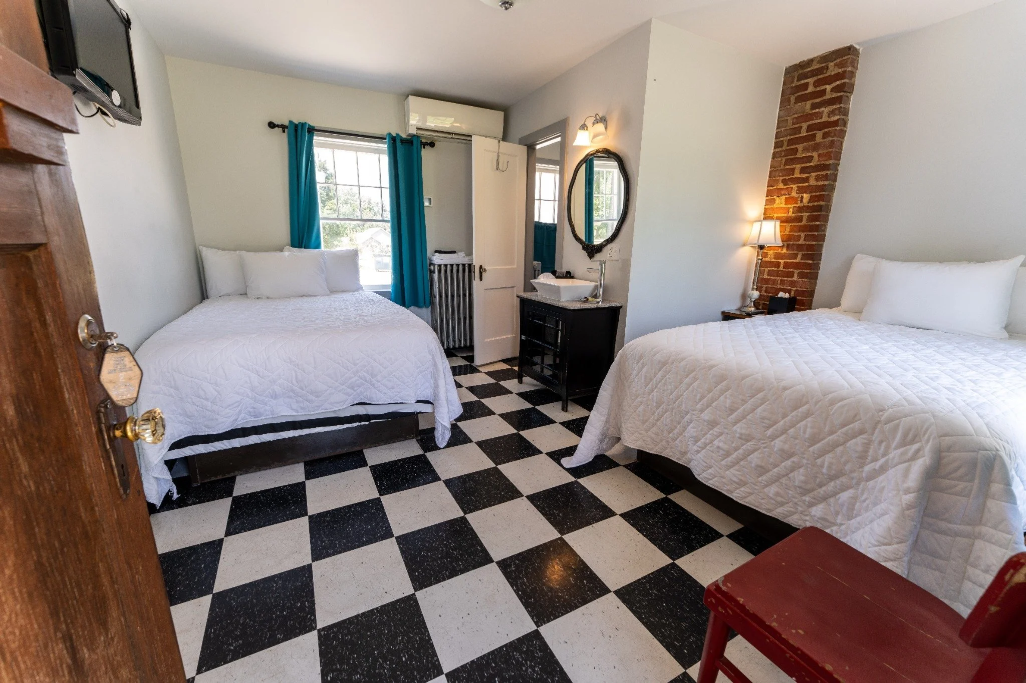 Restored Wagon Wheel Motel guest room with two beds, black-and-white tile, exposed brick, and teal accents.