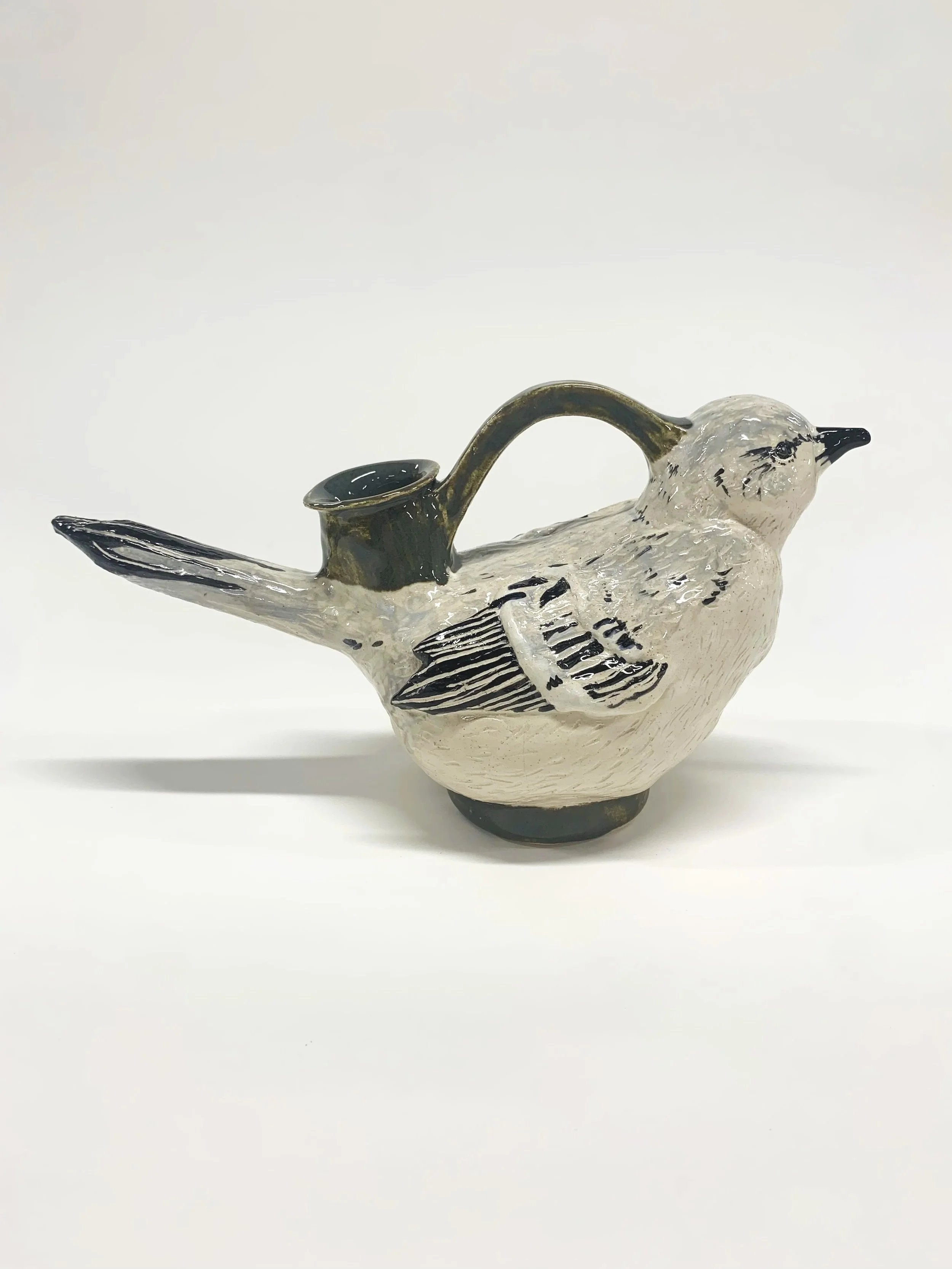 Ceramic mockingbird-shaped askos and painted feathers detail, against a white background.