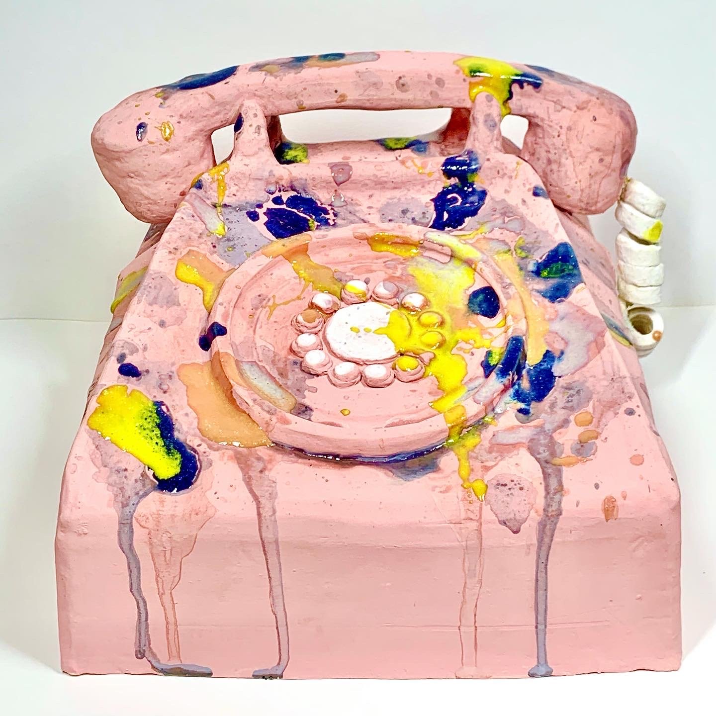 Pink-painted vintage rotary telephone with splashes of yellow, blue, and green paint, and glaze drips on a white background.