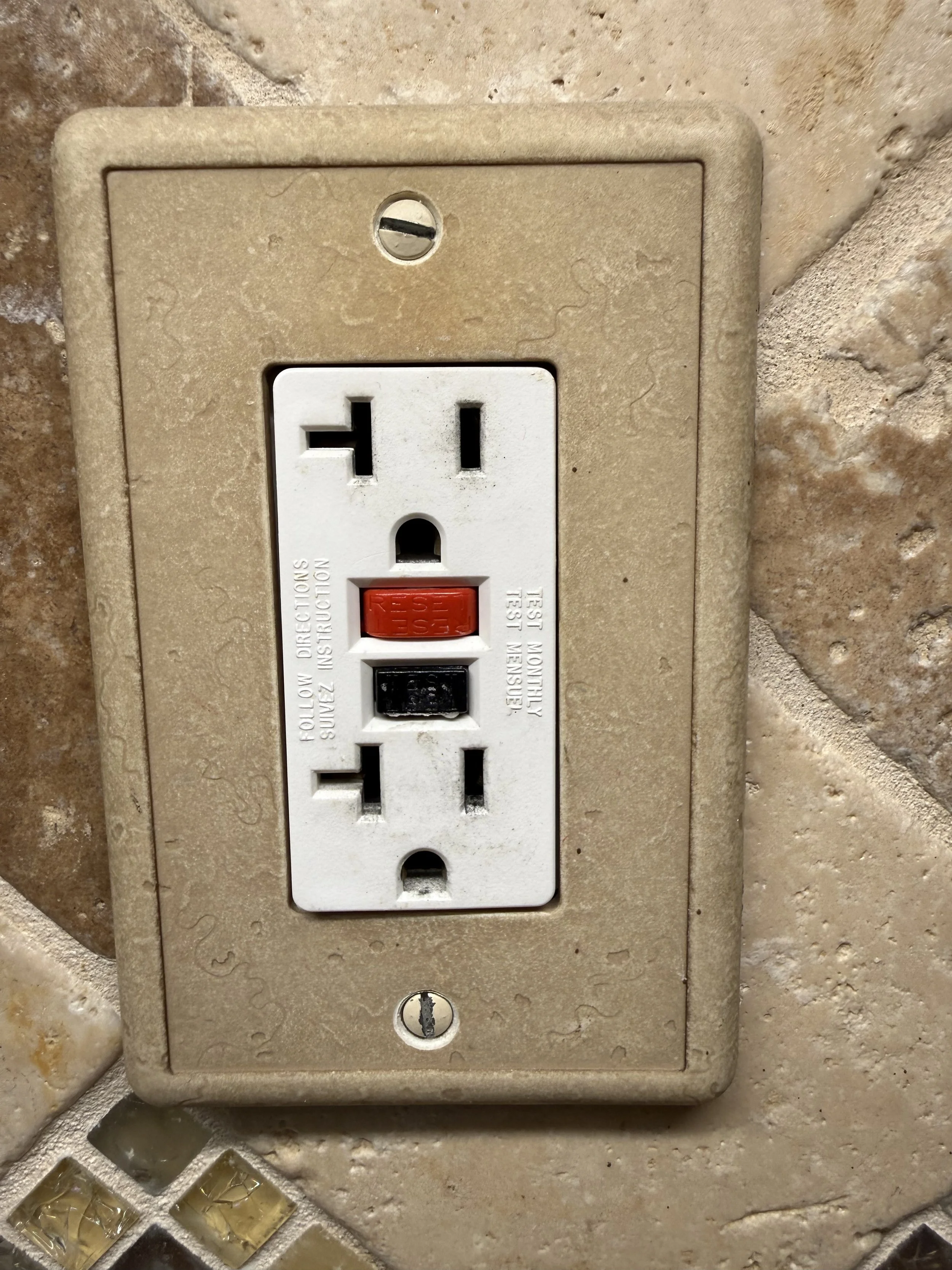 A beige electrical outlet with a child safety cover and a screw on the top and bottom, mounted on a textured wall.