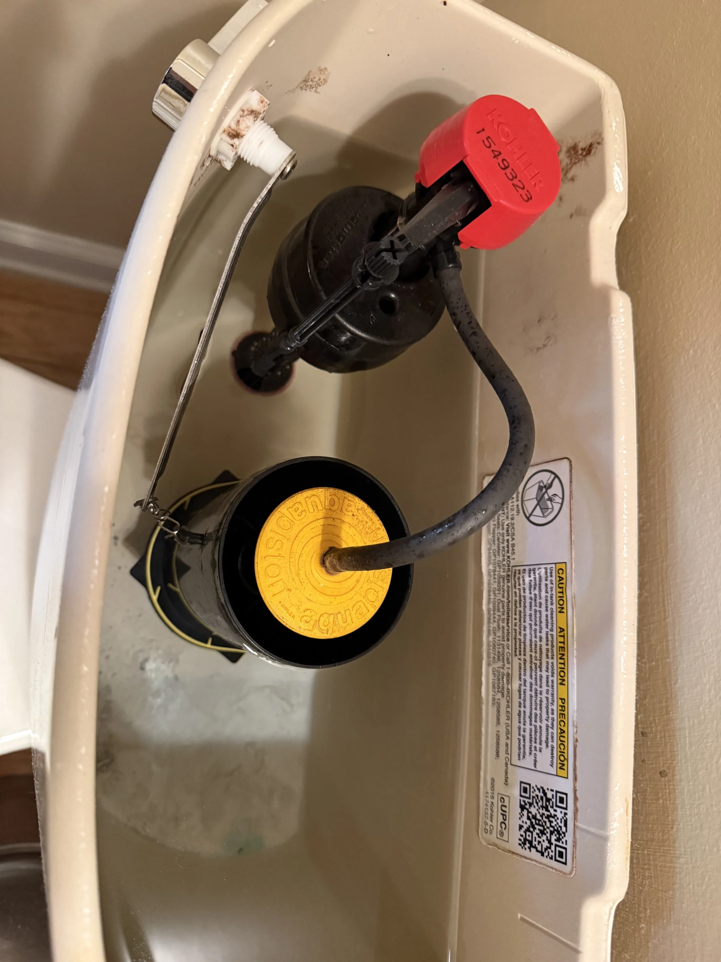An open water heater tank with a black heating element visible, and a red cap on top of the heating element, with a yellow caution sticker and a QR code on the side of the tank.