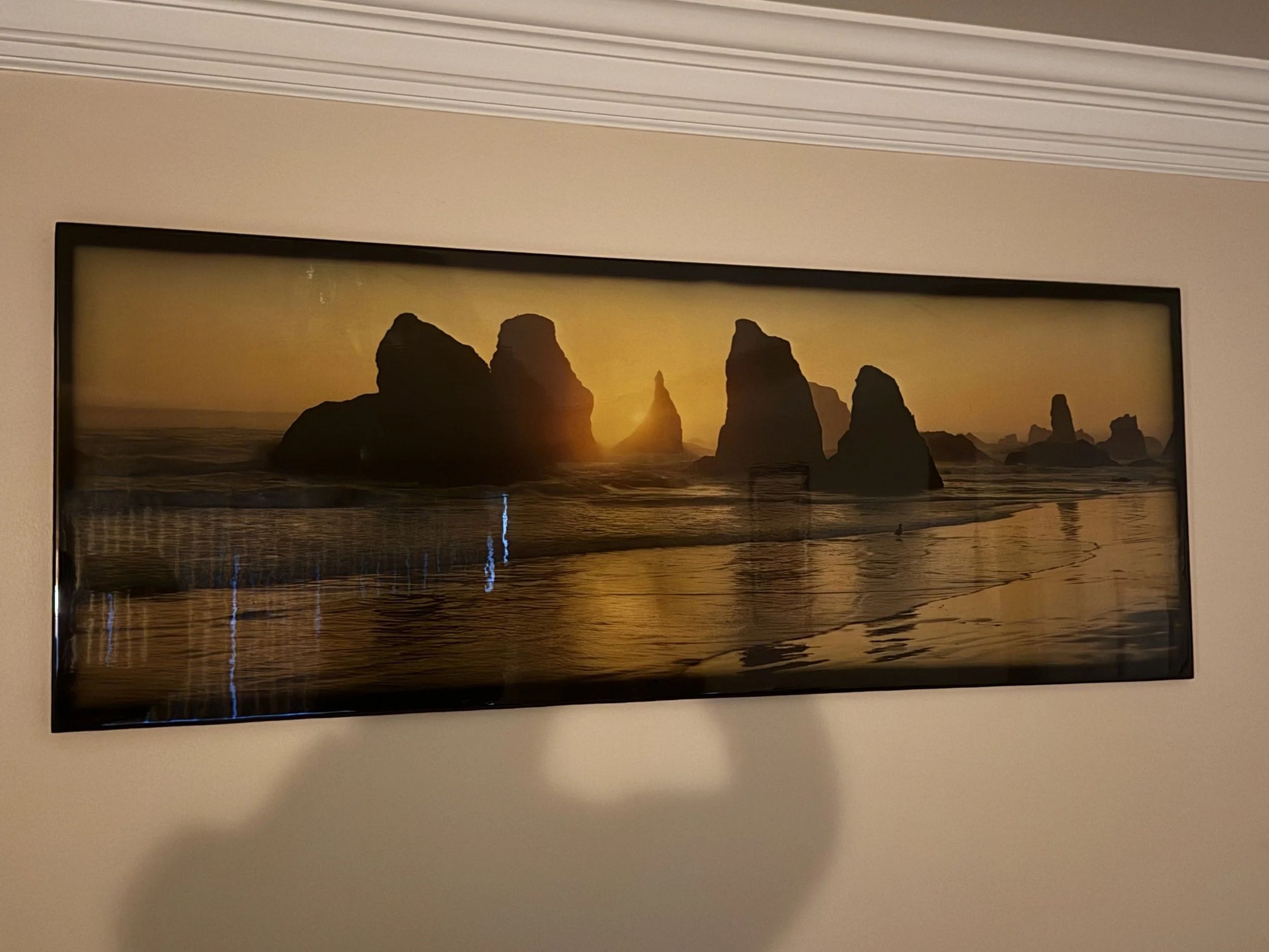 Framed landscape photograph of sea stacks at sunset, mounted on a wall.