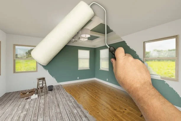 Person painting a living room wall with a paint roller, changing the wall color from white to green, with windows showing an outdoor scene.