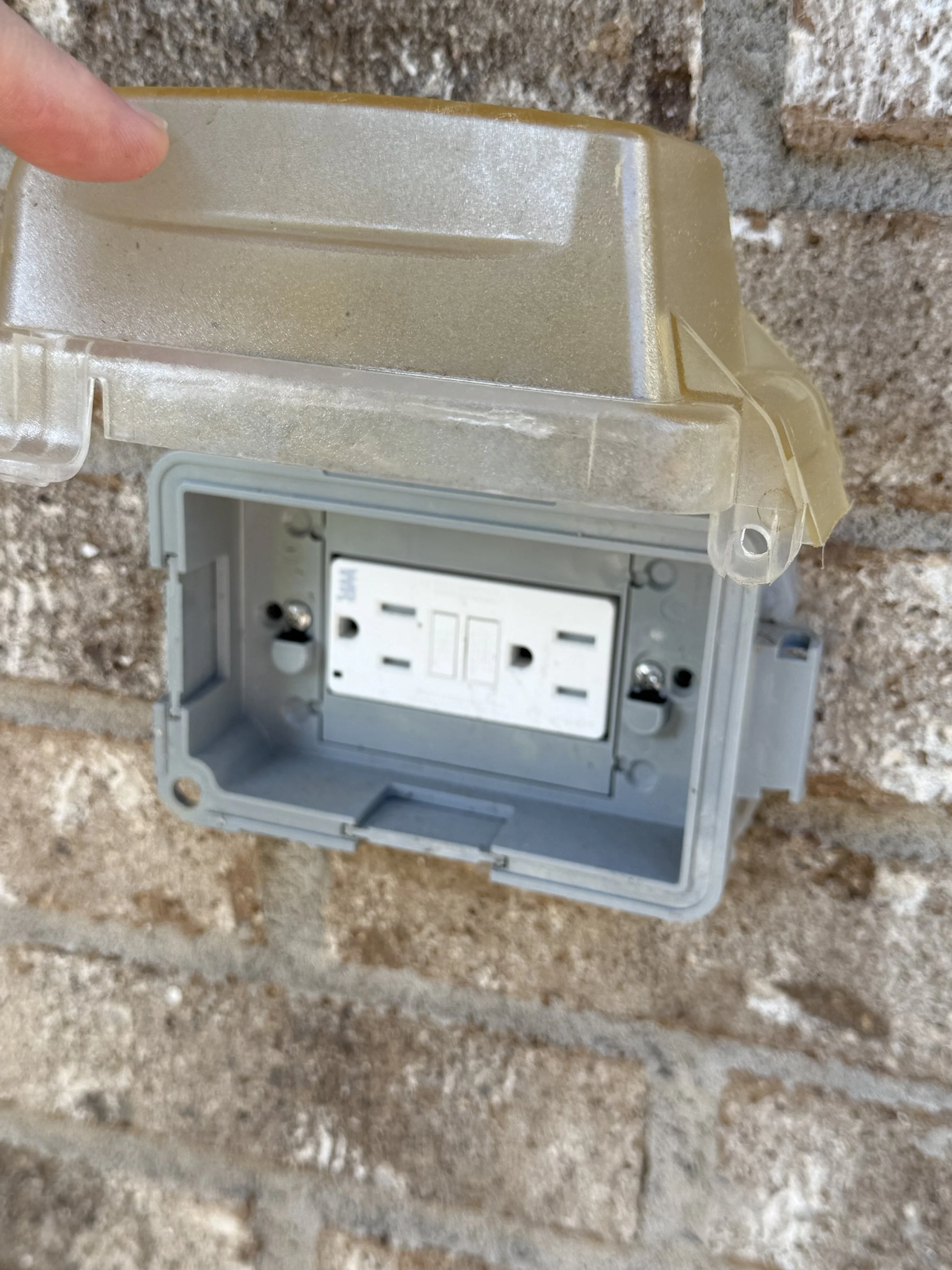 Close-up of an outdoor electrical box with the cover removed, mounted on a brick wall with visible dirt and dust deposits.