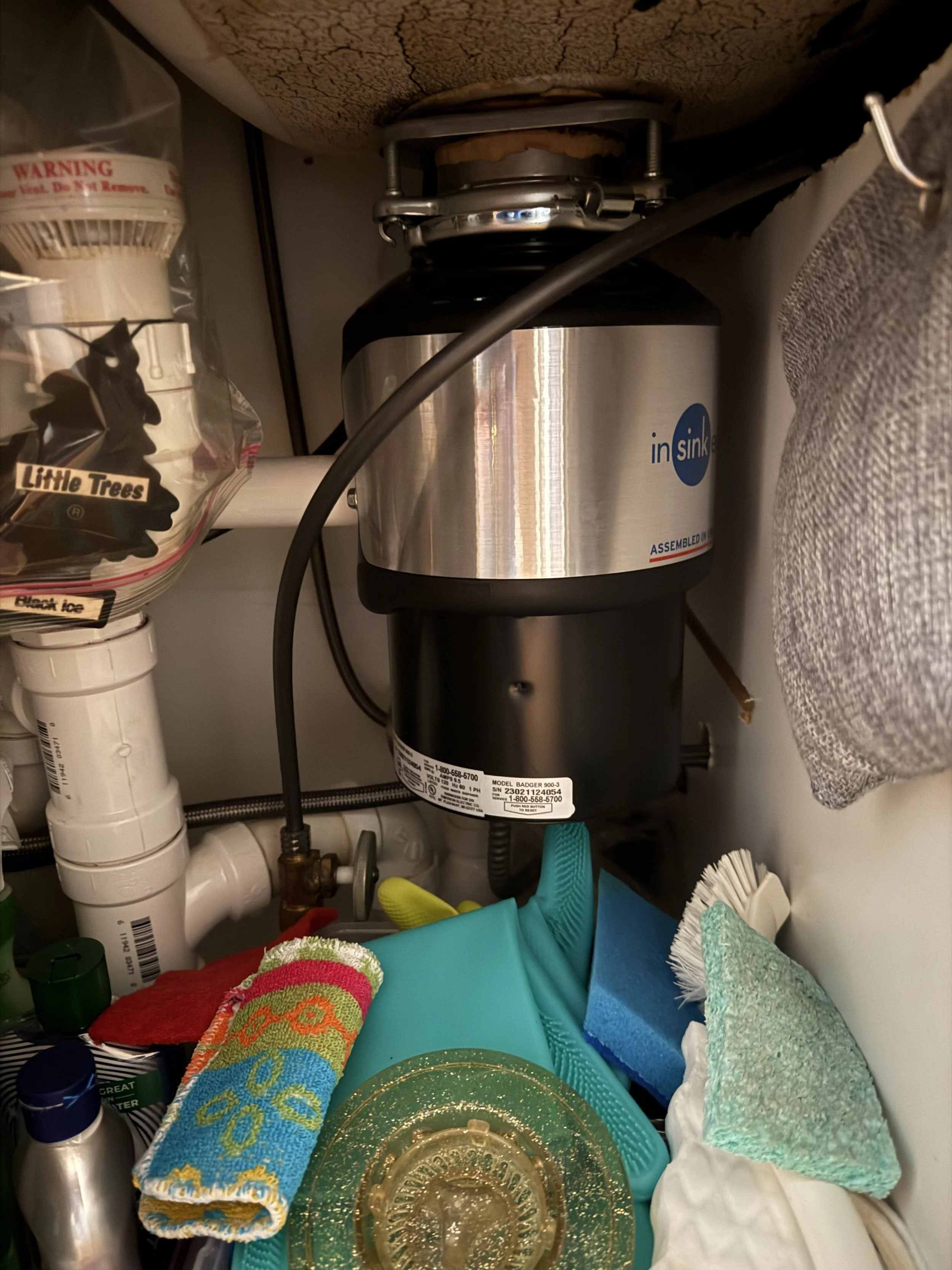 Plumber's sink cabinet with various cleaning supplies, towels, and a garbage disposal unit. The image shows towels, a plastic falcon decorative dish, and plumbing parts.