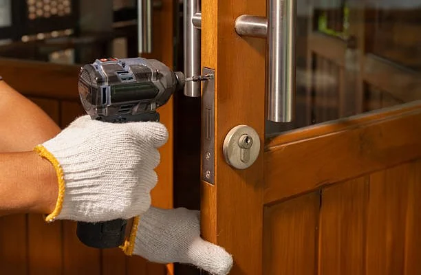 Person installing a lock on a wooden door with a cordless drill.