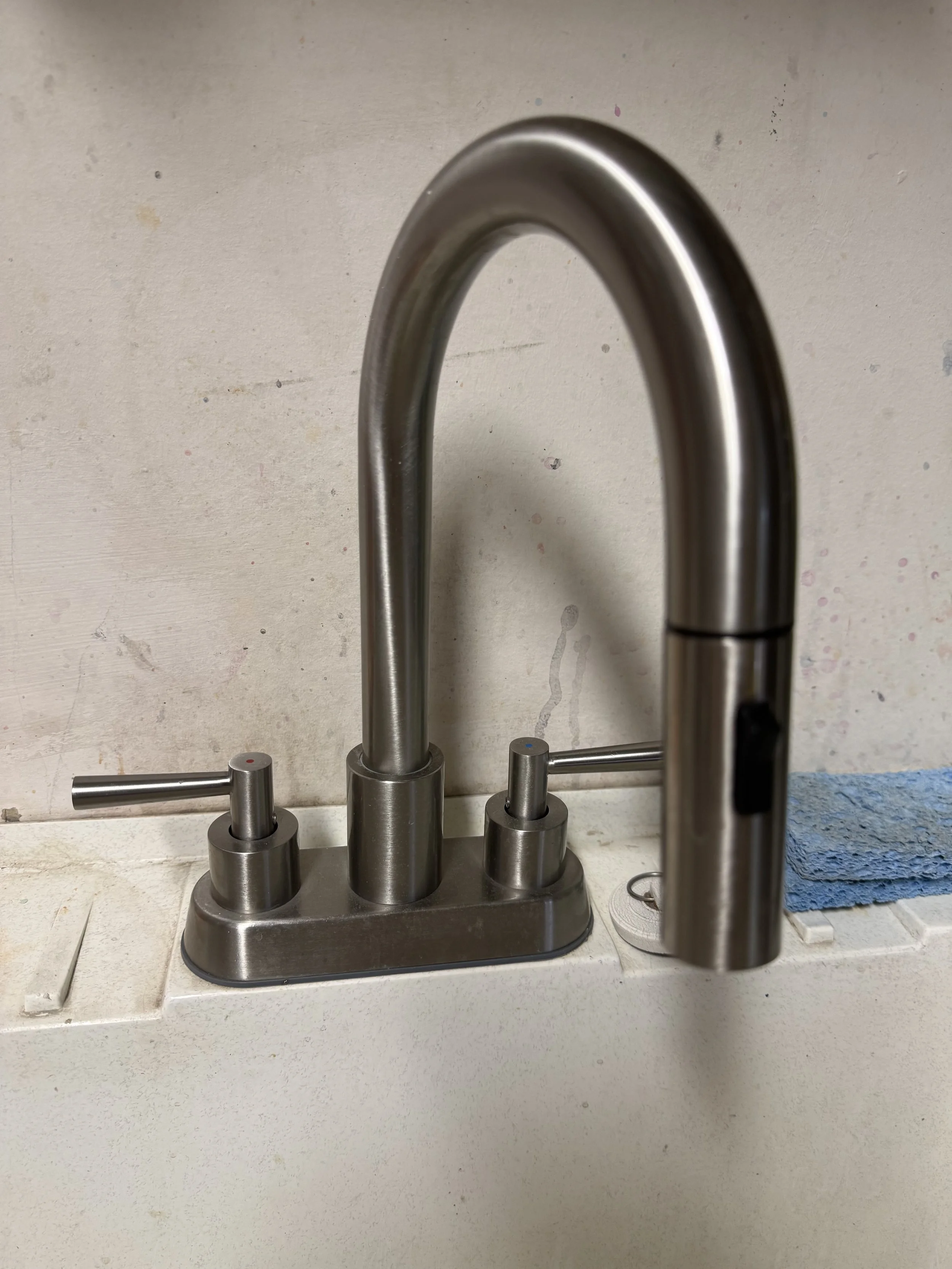 Stainless steel kitchen faucet with two handles on a white countertop, next to a blue towel and a roll of paper towels.
