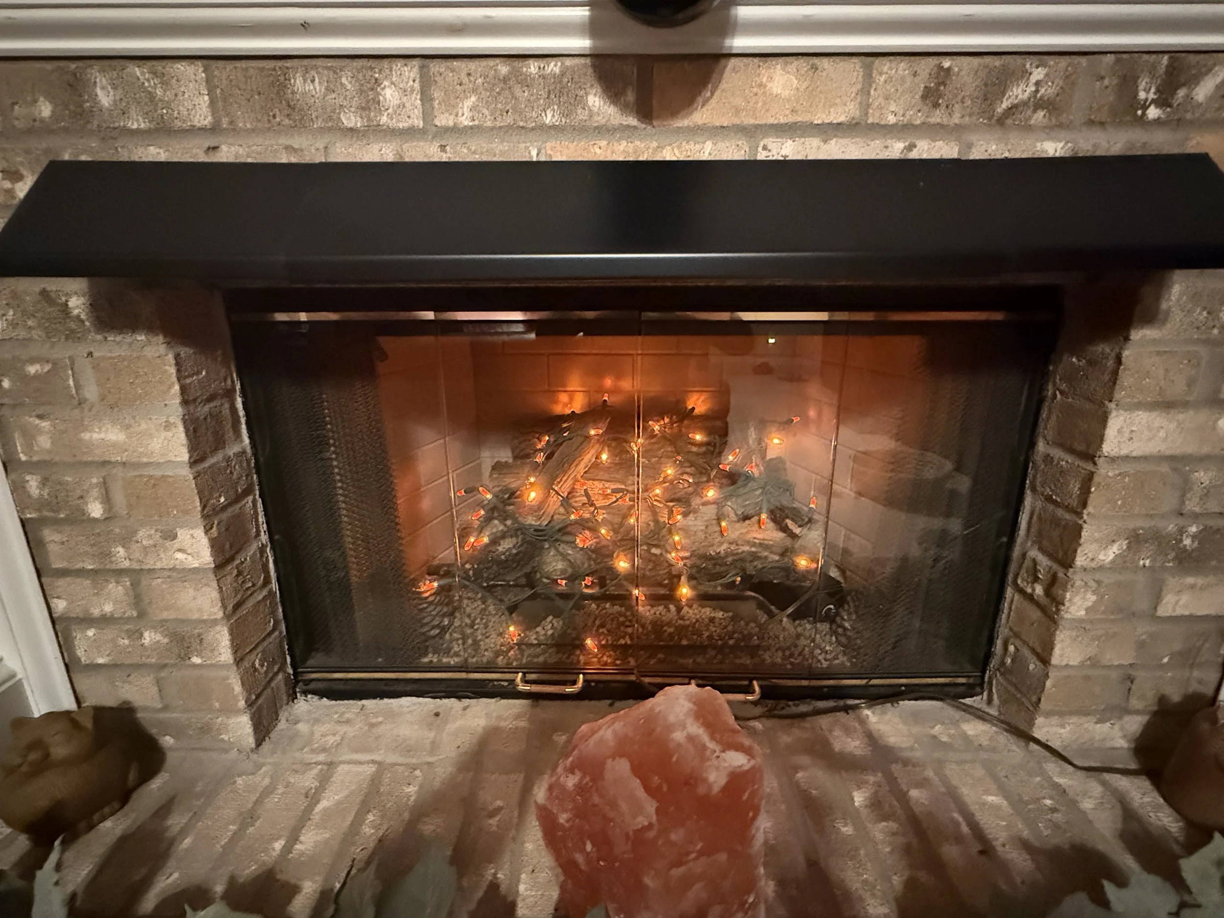 Fireplace with brick surround and black metal hood, glowing with orange embers and some logs inside.