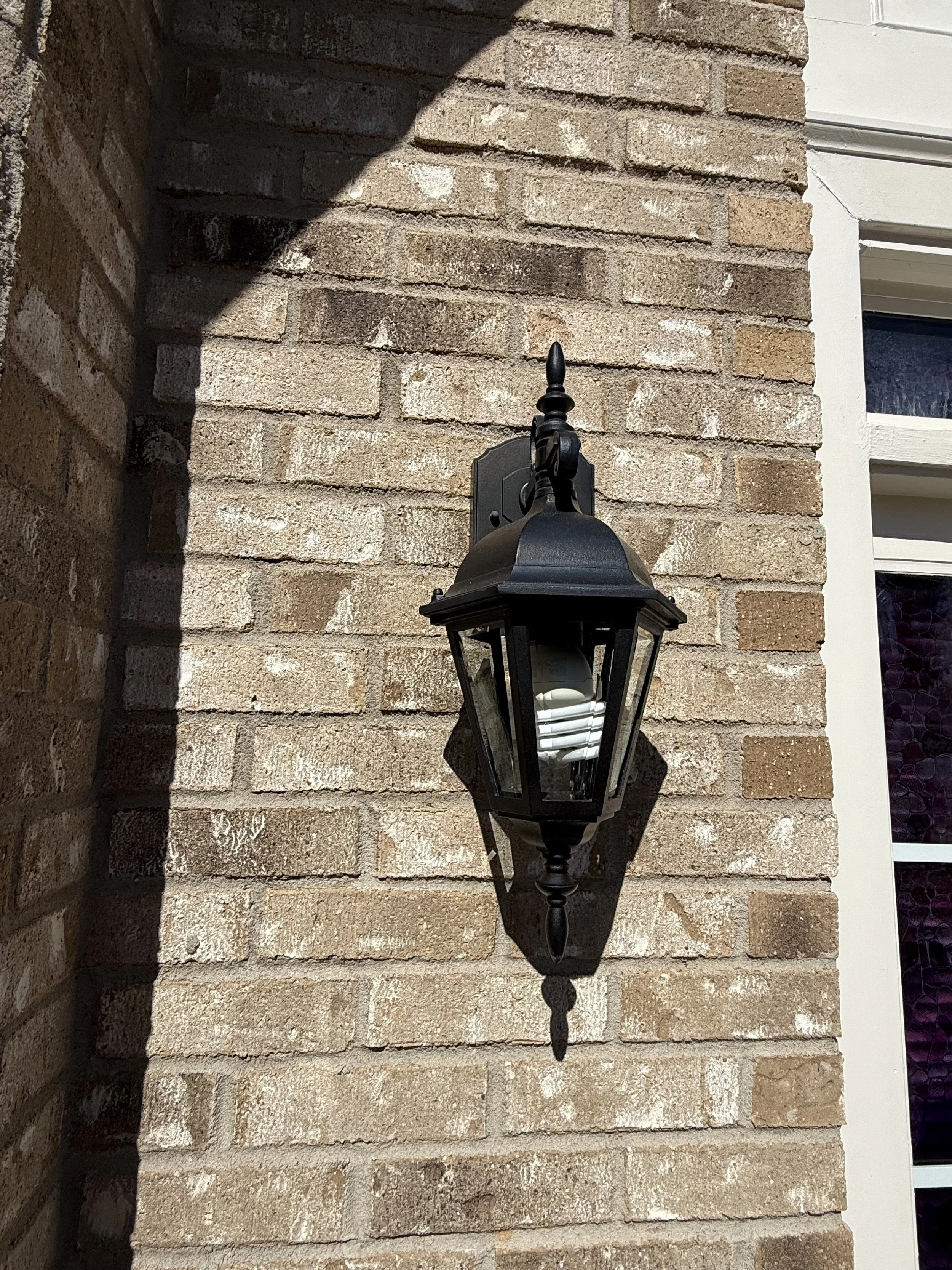 An outdoor wall light fixture attached to a brick wall next to a window.