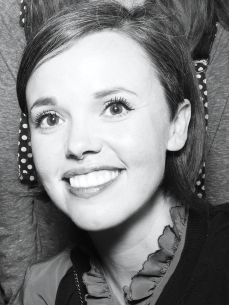 A head shot of a woman with short hair, a septum piercing, bright eyes, smiling.