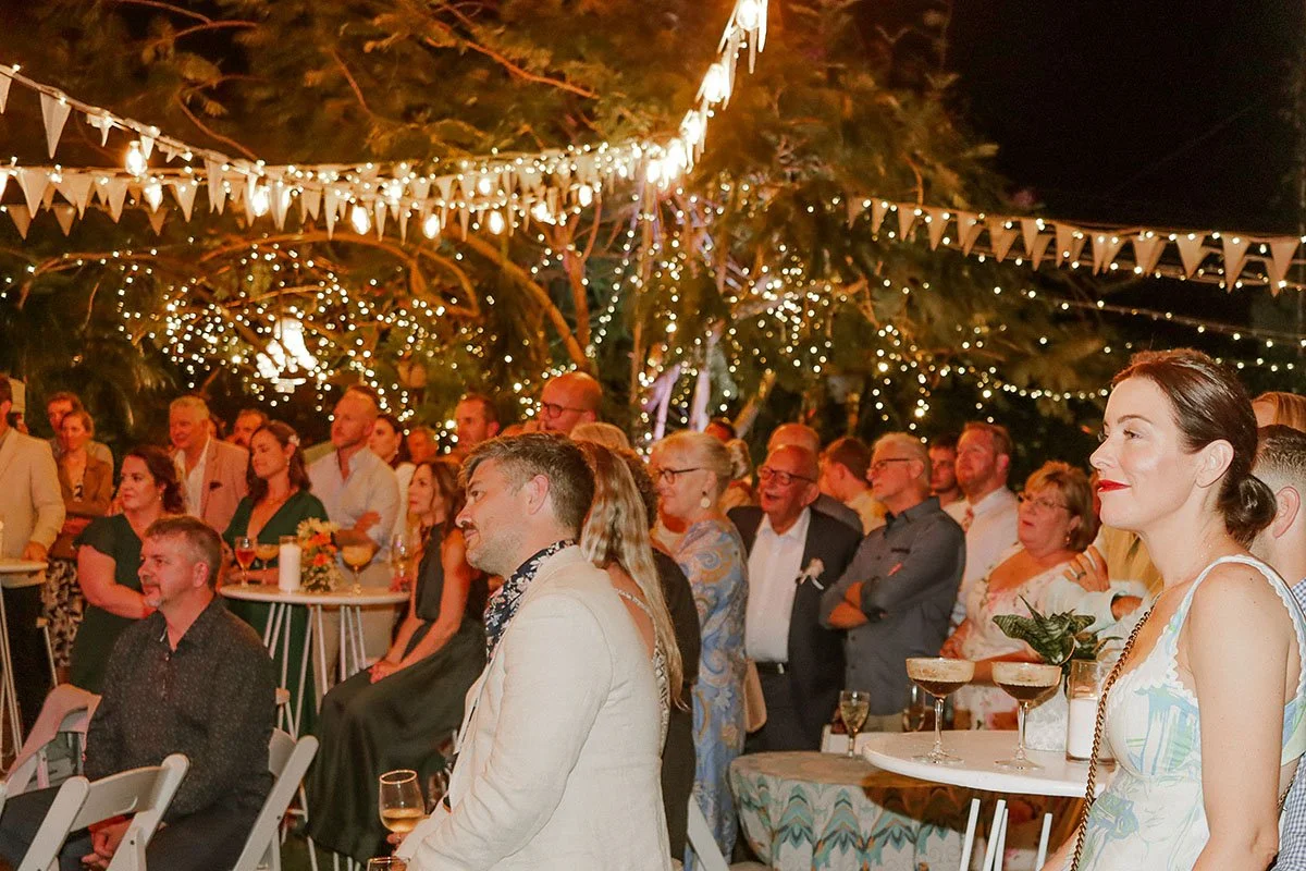 People gathered at an outdoor nighttime event decorated with string lights and bunting, enjoying the celebration.