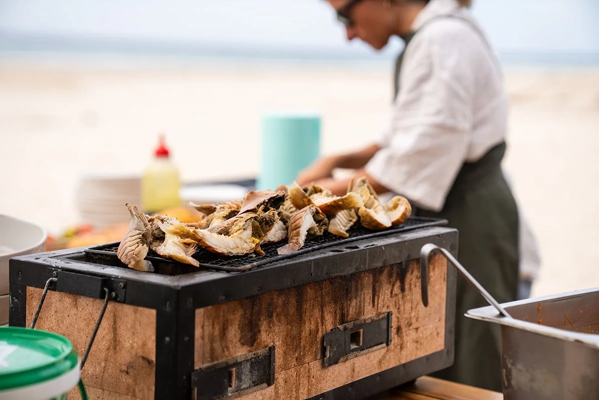 Person grilling fish on a barbecue grill at the beach.