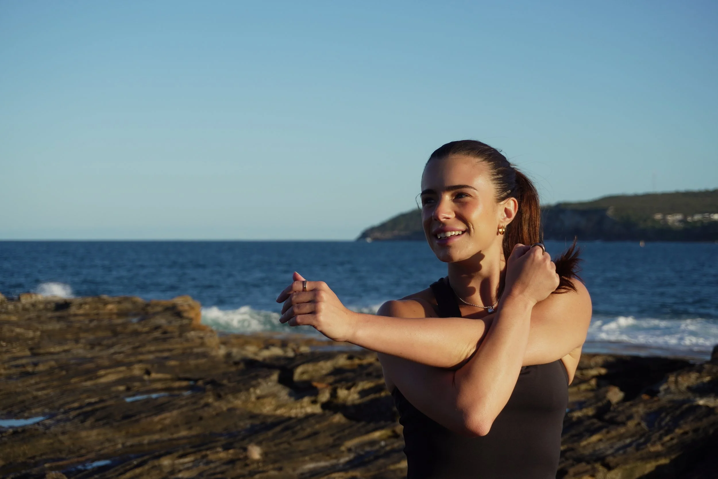 Maddi from The Radiant smiling and stretching by the ocean