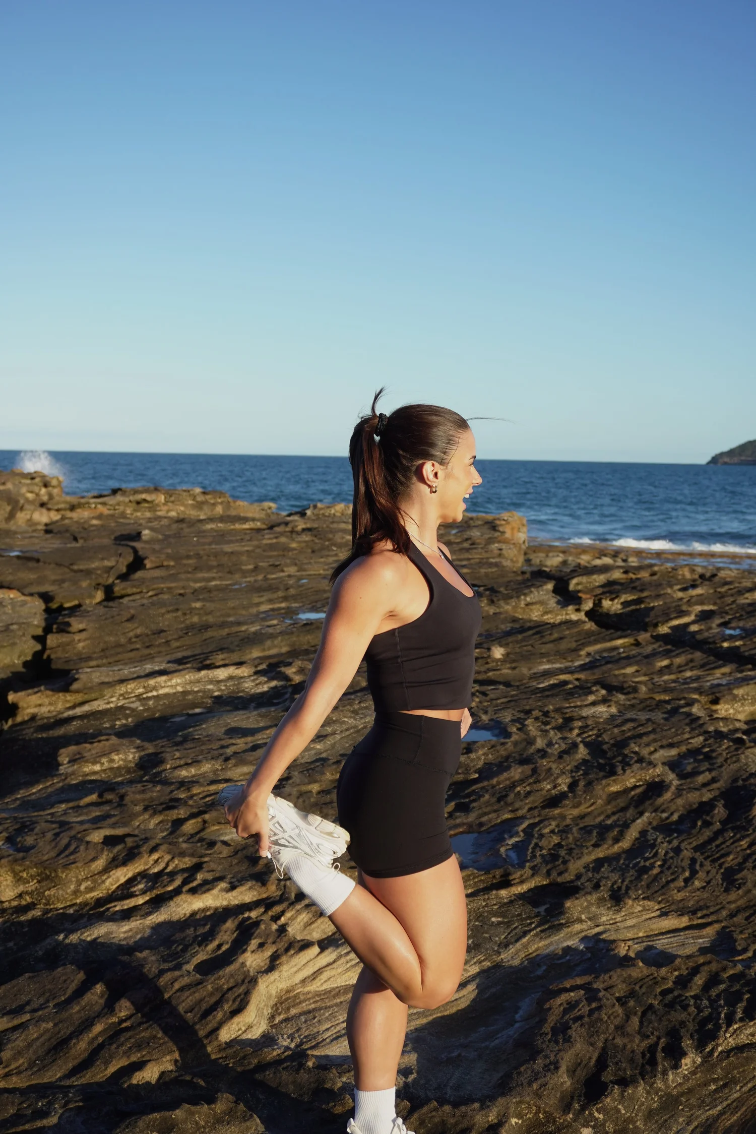 Maddi stretching her quad on the rock shelf by the ocean