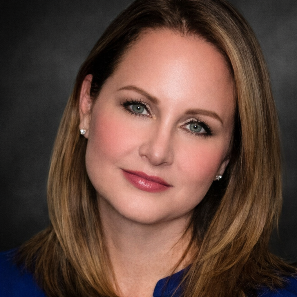 Close-up portrait of a woman with light brown hair, blue eyes, and light makeup, wearing earrings and a blue top, against a dark background.