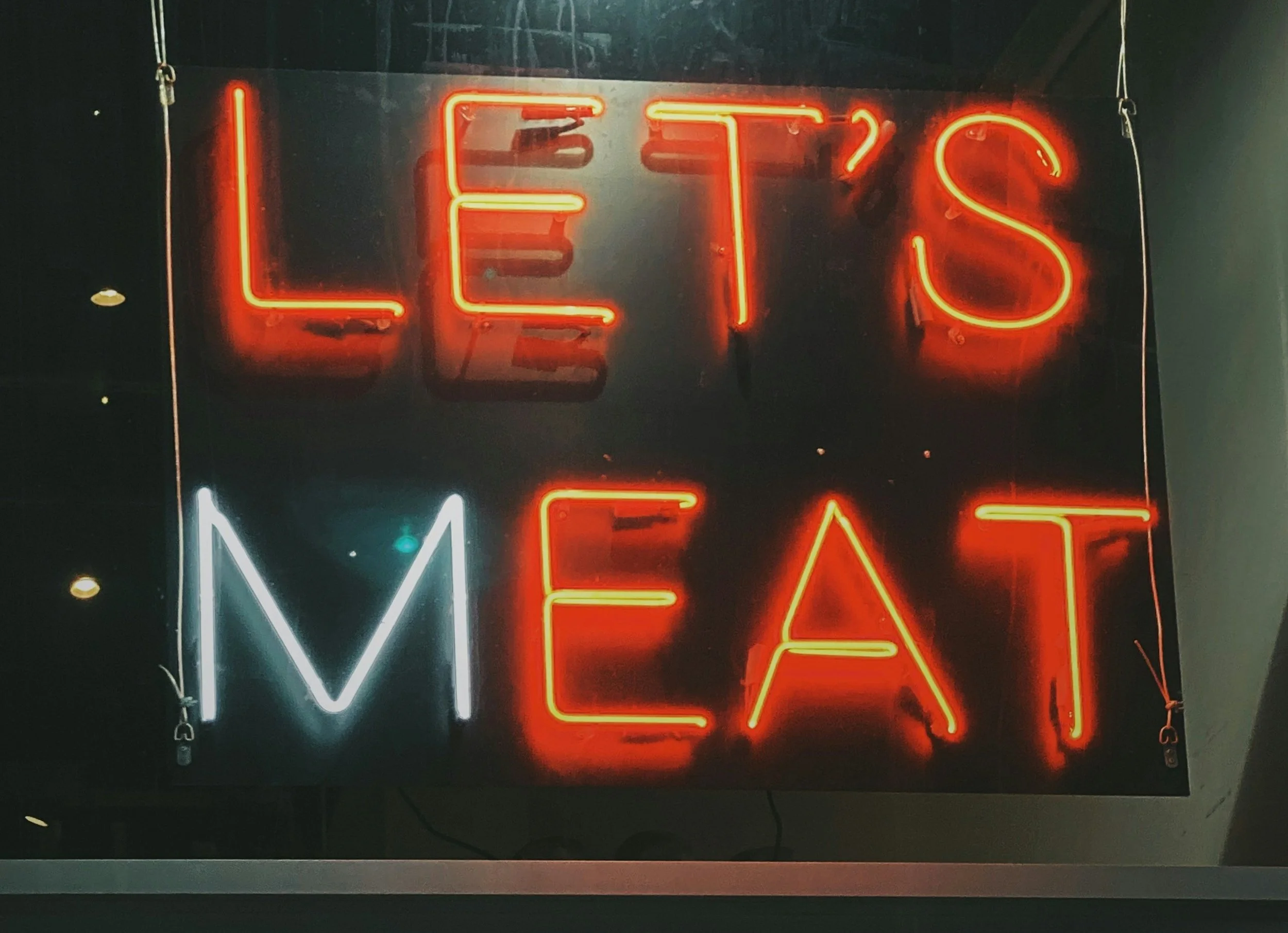 Neon sign that says 'LET'S MEAT' with 'LET'S' in red and 'MEAT' in white and red neon lights.