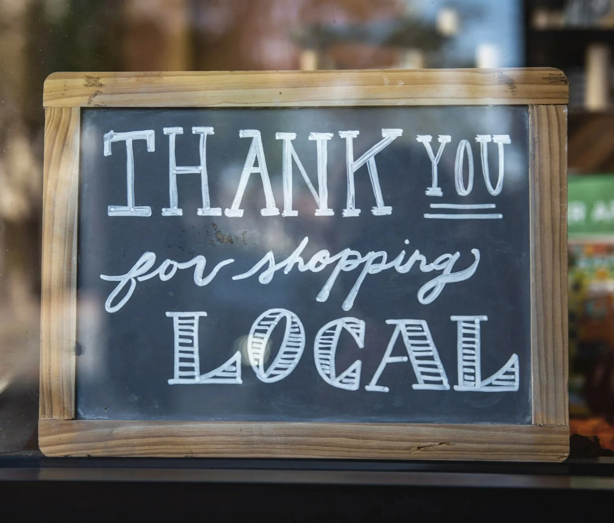A chalkboard sign with wooden frame reads 'Thank You for shopping Local' in white handwritten text.