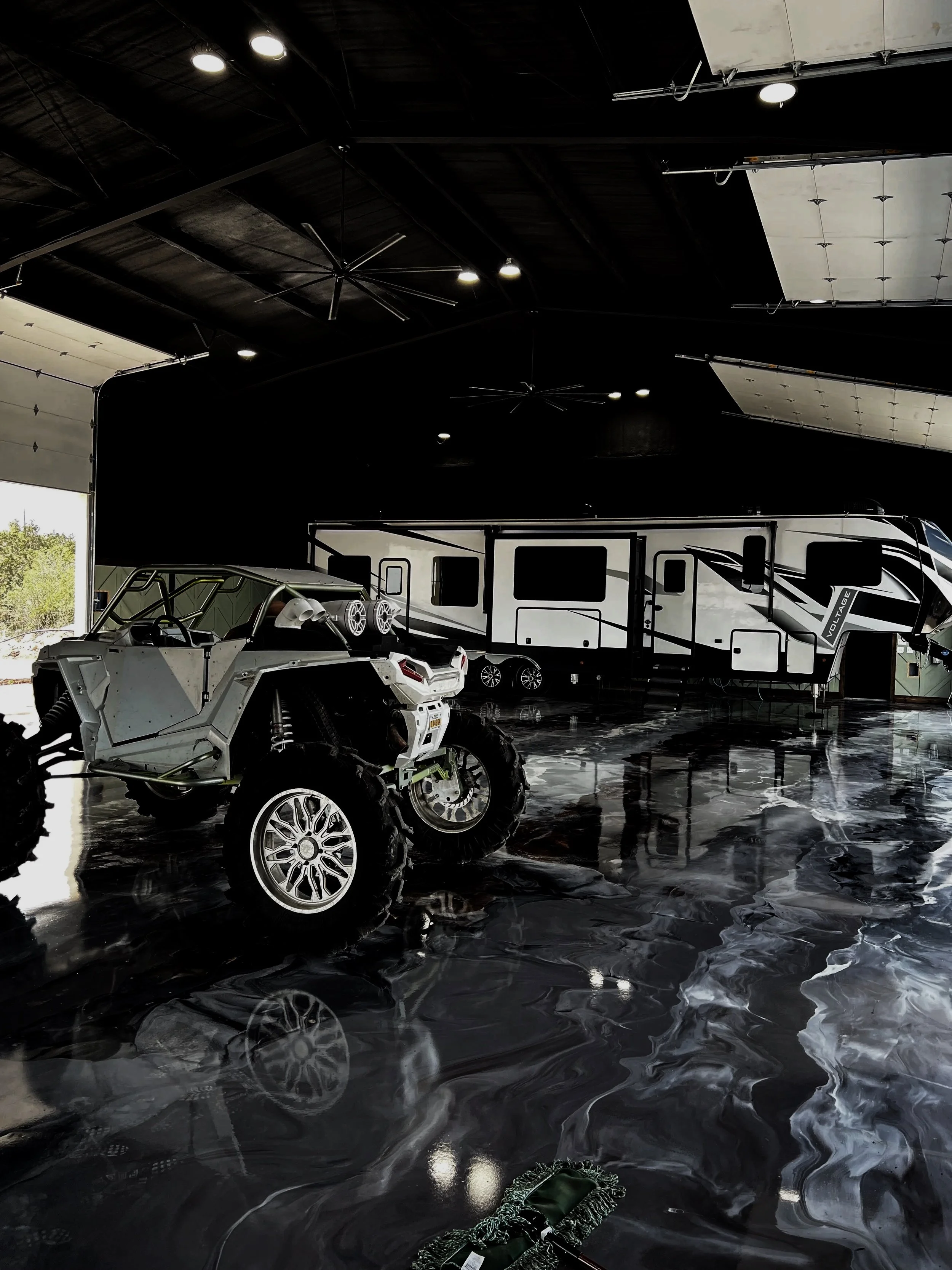 A garage with a black marble floor, a small white off-road vehicle, and a large black and white RV.