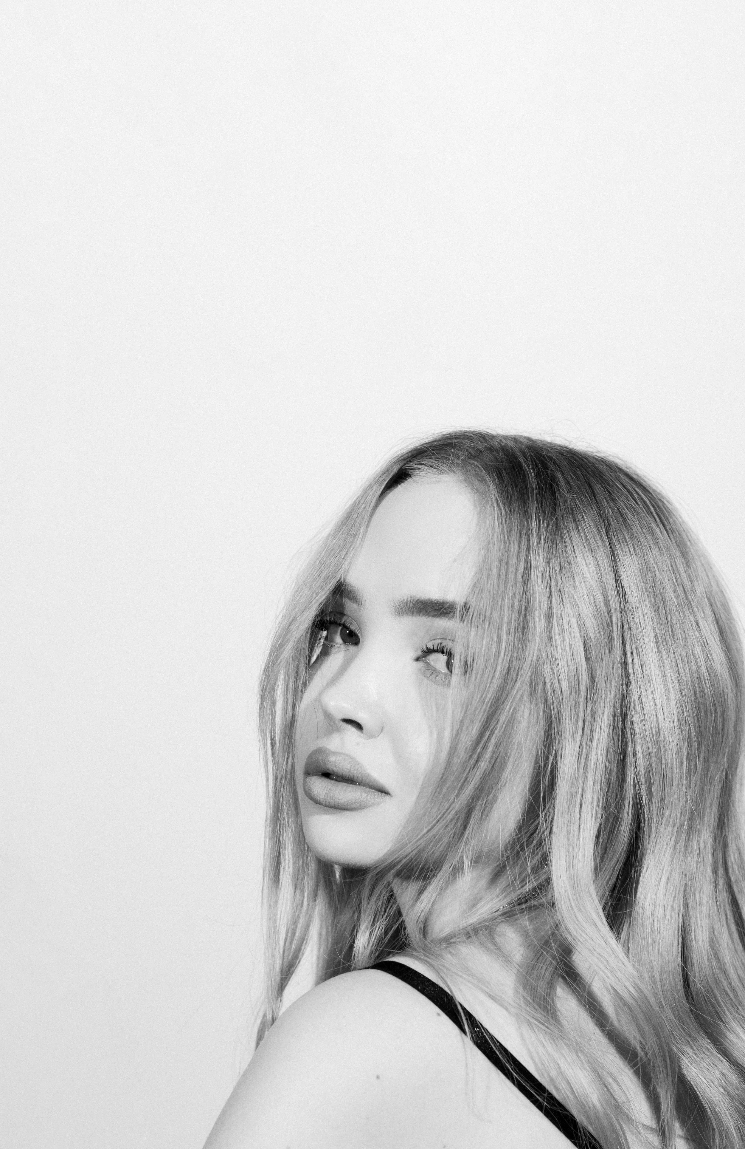 Black-and-white portrait of a woman with long, wavy hair, looking to her right, with serious expression, against a plain light background.