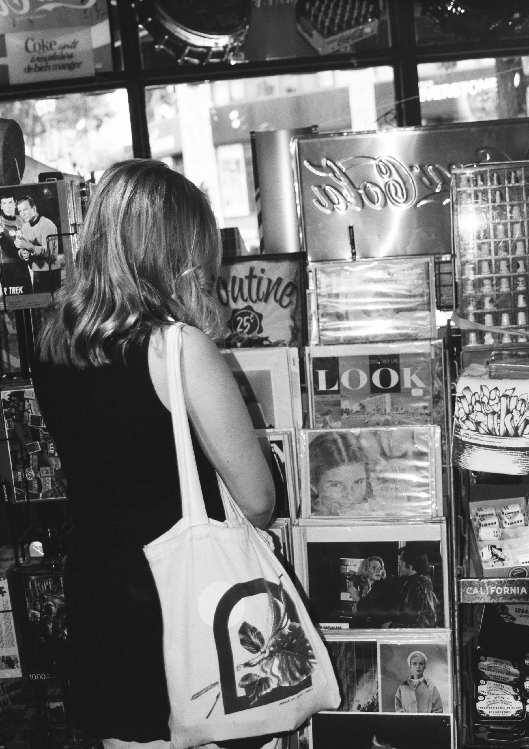 A woman with shoulder-length wavy hair shopping at a magazine stand inside a store.
